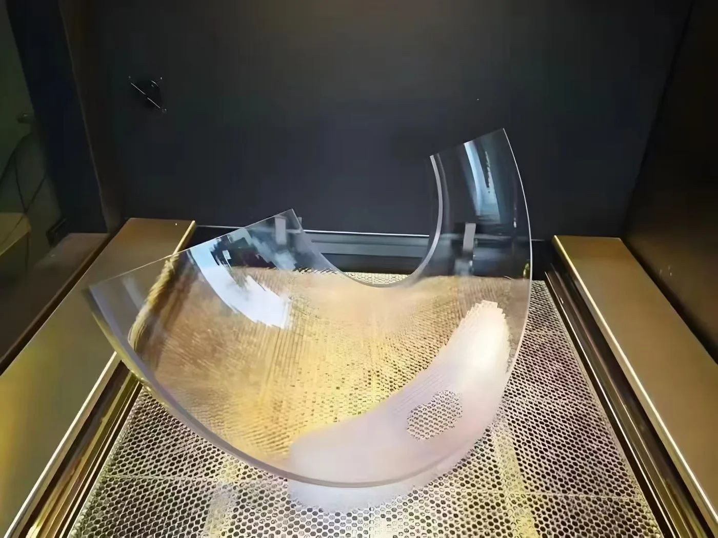 A large clear SLA resin part, curved like a shallow scoop, on the printer bed.